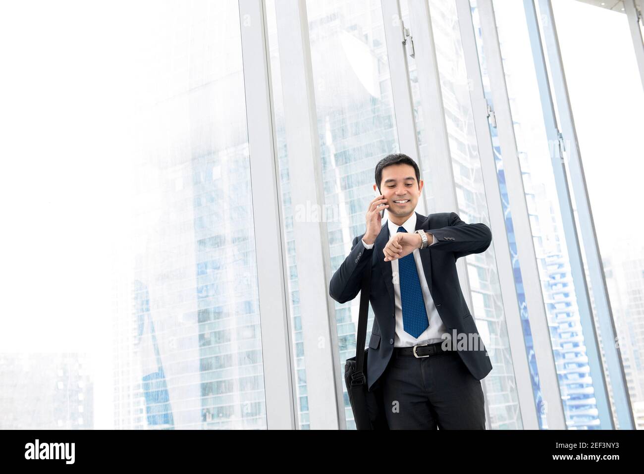 Geschäftsmann beobachten die Zeit und telefonieren auf Handy, während Zu Fuß auf dem Flur des Gebäudes Stockfoto