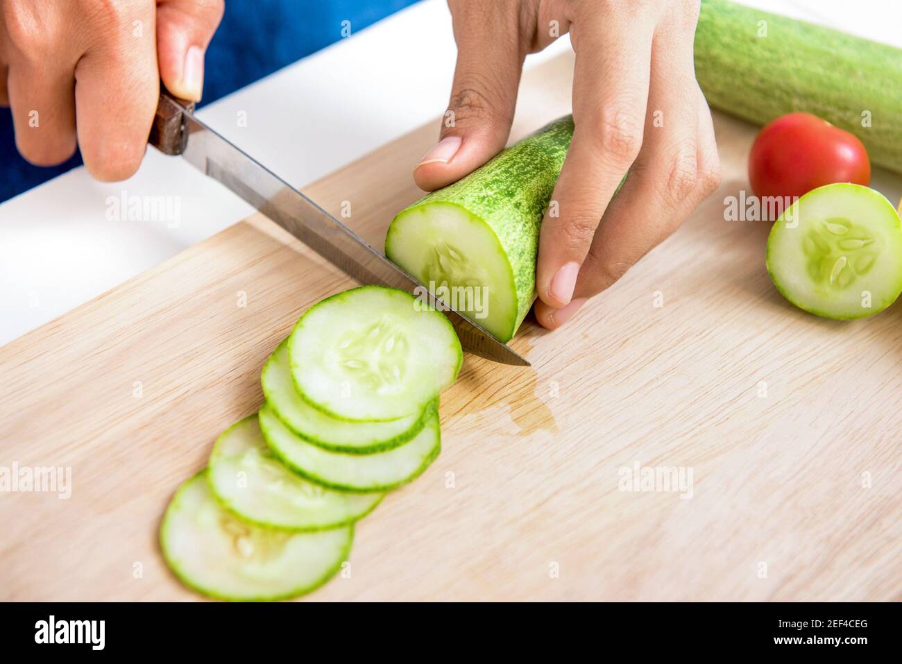 Gurke wird von einem Messer auf Holzschneidebrett geschnitten Stockfoto