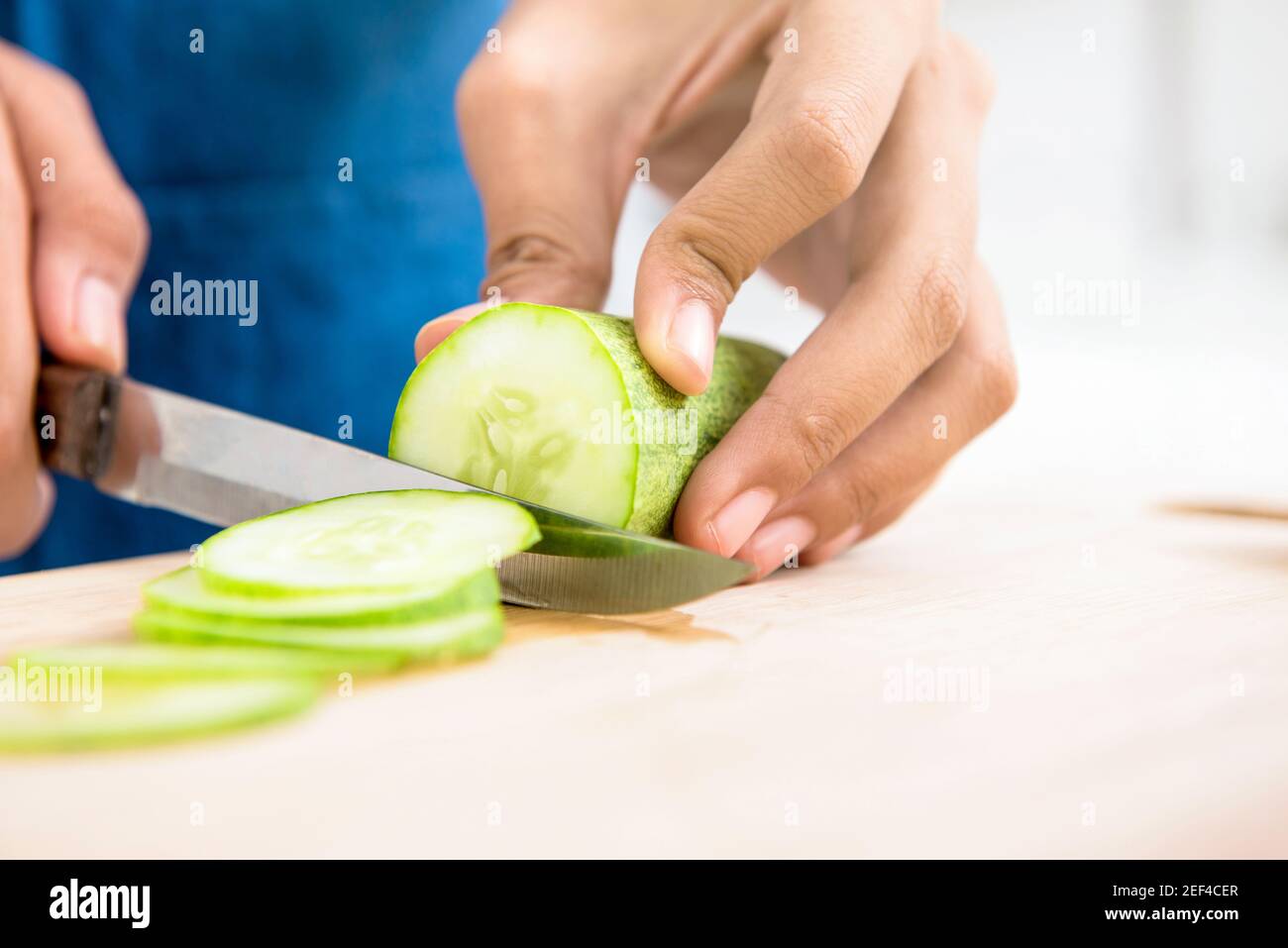 Gurke wird von einem Messer auf Holzschneidebrett geschnitten Stockfoto