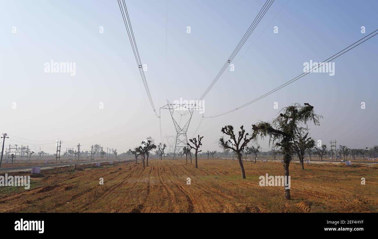 10. Februar 2021- Sikar, Jaipur, Indien. Desolate leere Felder mit dreiphasigen Stromversorgungsleitungen. Drahtfalle führt zum Horizont mit blauer Himmel Natur. Stockfoto