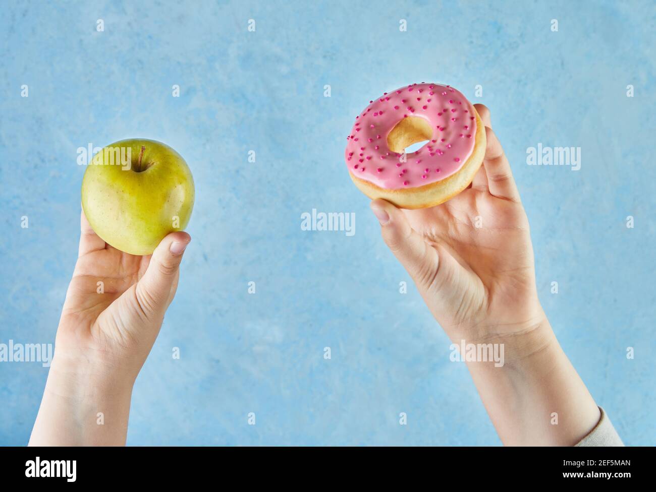 Kinderhände mit Apfel und Donut auf blauem Hintergrund. Stockfoto