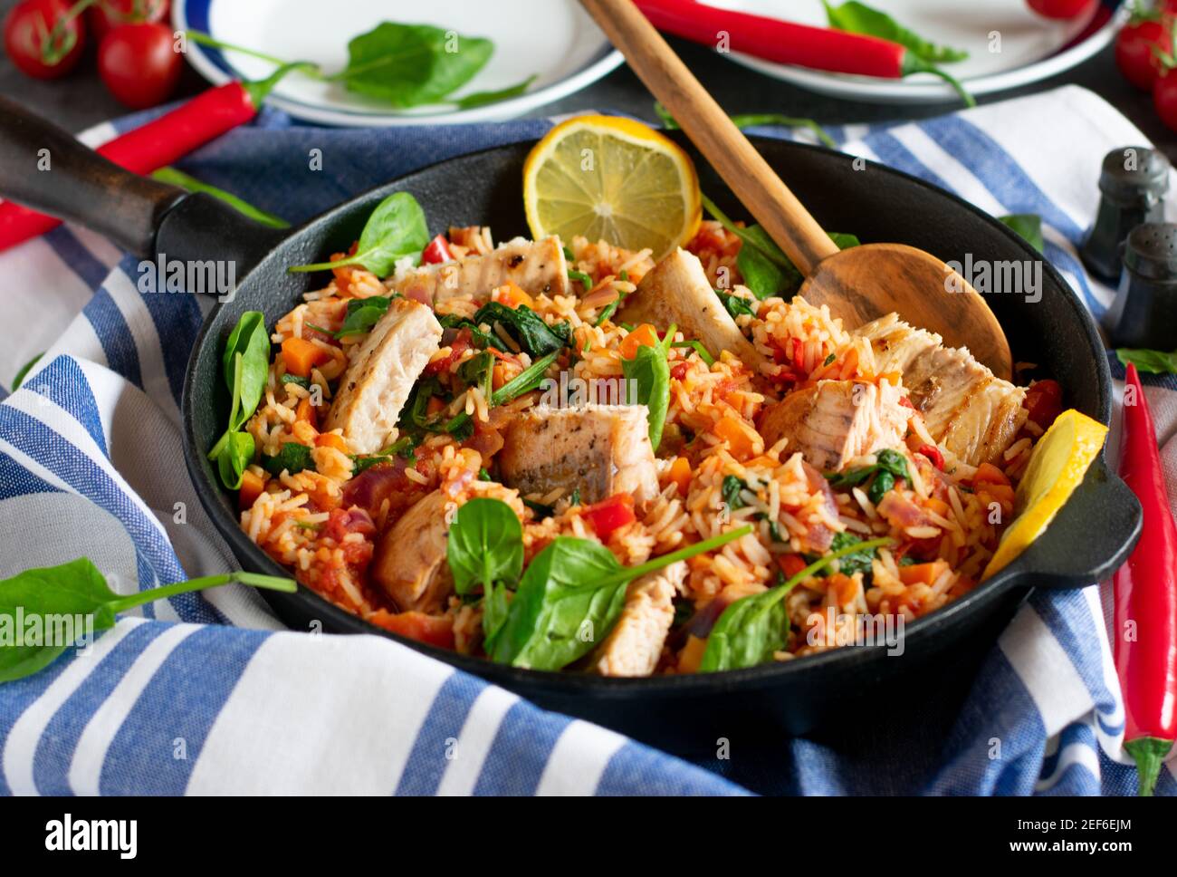 mediterranes Fischgericht mit gebratenem Fisch, Reis und würzigem Gemüse in einer rustikalen Pfanne auf einem Tisch serviert Stockfoto
