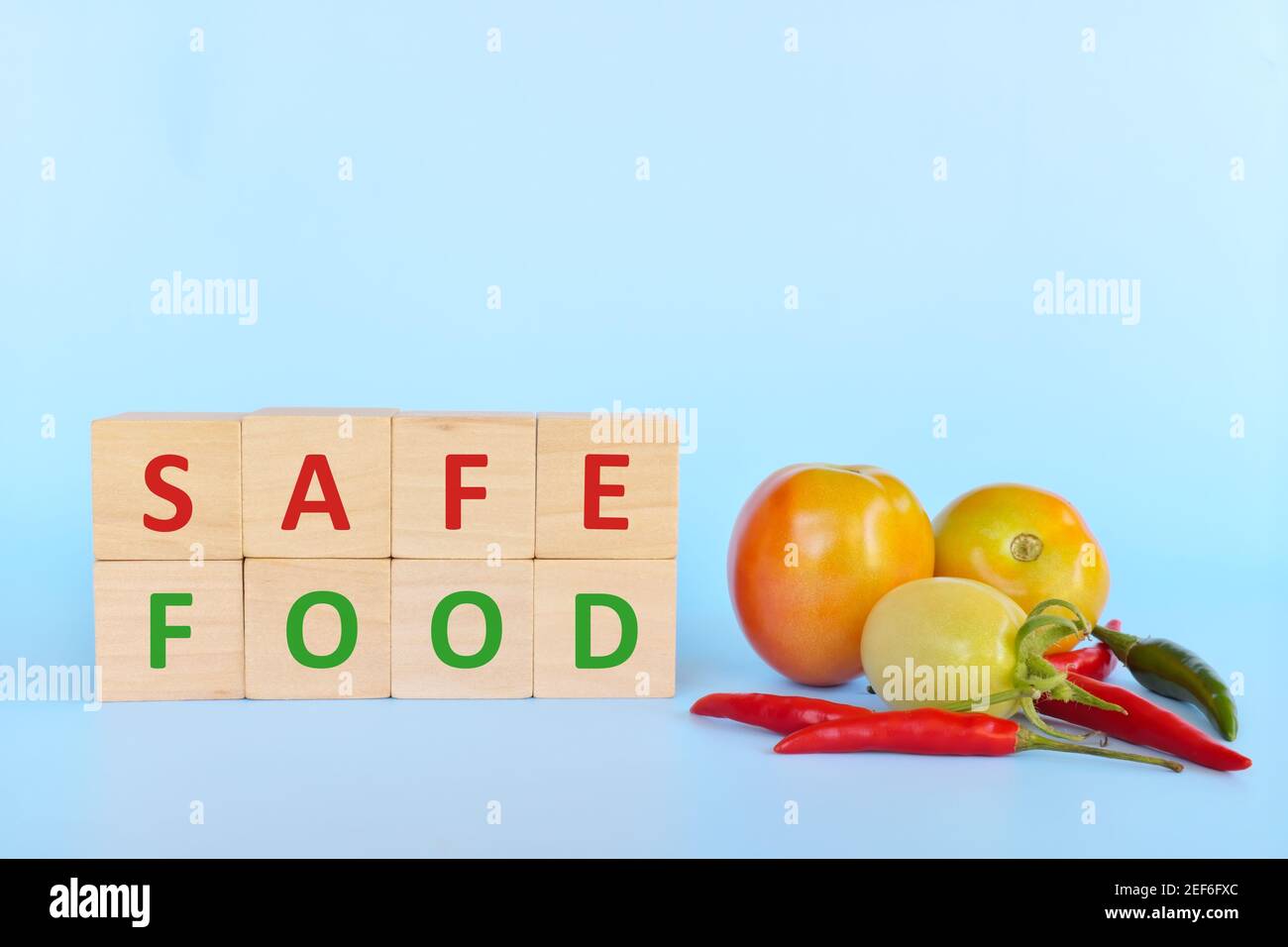 Sicheres Lebensmittelkonzept. Tomate und Holzklötze mit Word Safe Food auf blauem Hintergrund mit Kopierraum. Stockfoto