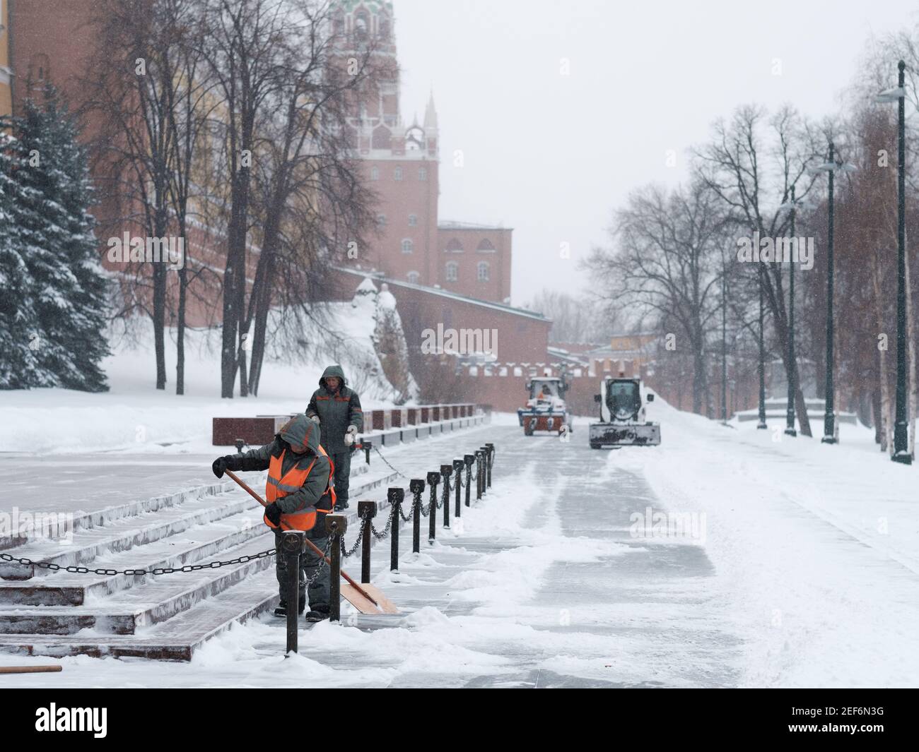Moskau. Russland. Februar 12, 2021. Versorgungsarbeiter nutzen Schaufeln, um bei einem Schneefall in der Nähe der Kremlmauer Schnee zu räumen. Traktoren im Hintergrund sind Stockfoto