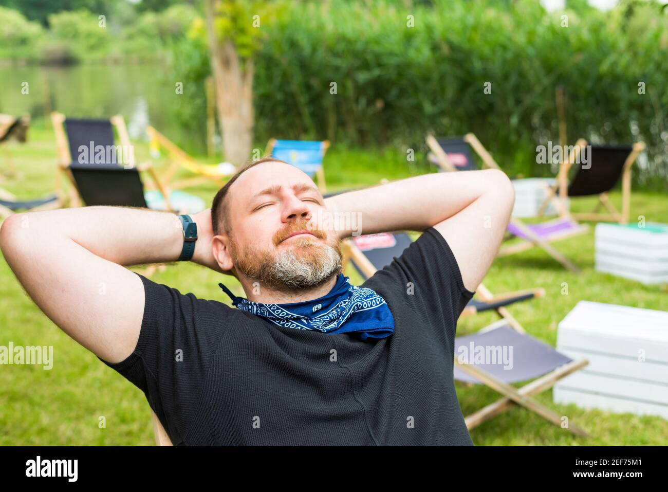 Erwachsene Mann entspannt im Freien in einer Stadt Strandgarten hält die Hände hinter dem Kopf. Solo Outdoor-Aktivitäten Stockfoto