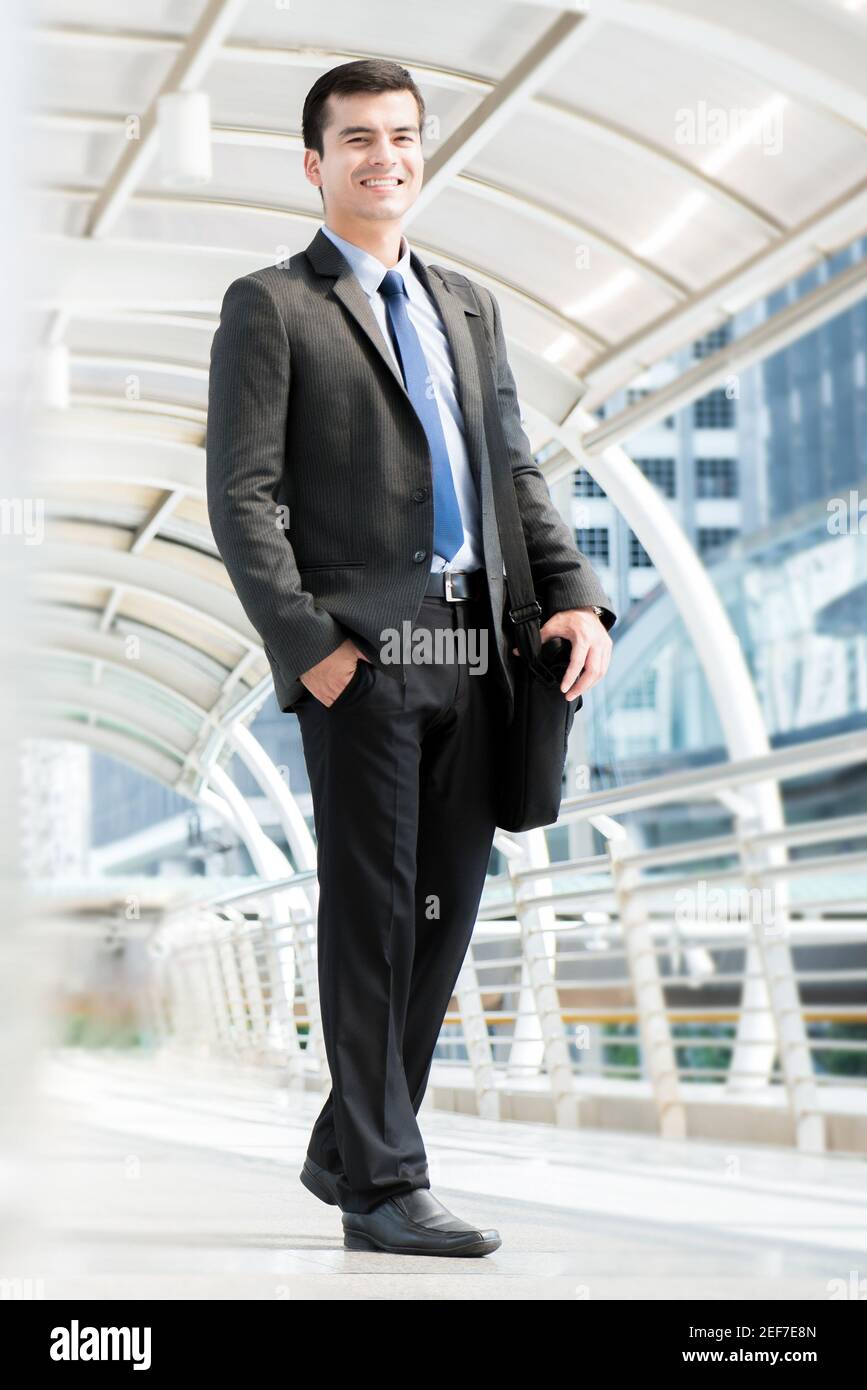 Lächelnder junger Geschäftsmann, der eine Tasche trägt, während er im überdachten Gang im Freien läuft, voller Körper Stockfoto