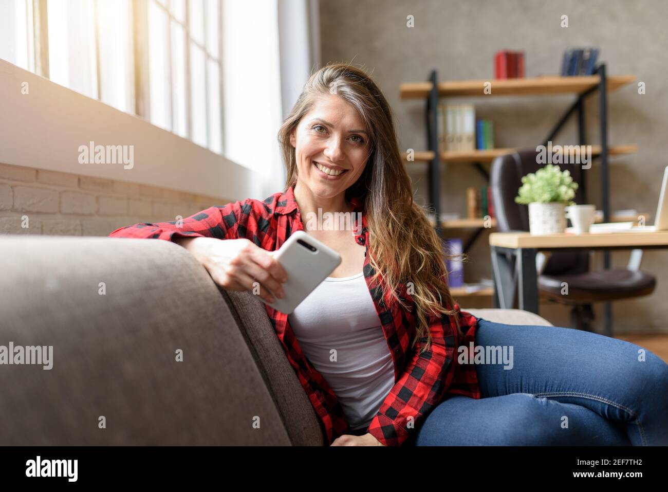 Lächelndes Mädchen, das sich mit ihrem Smartphone auf einem Sofa entspannt Stockfoto