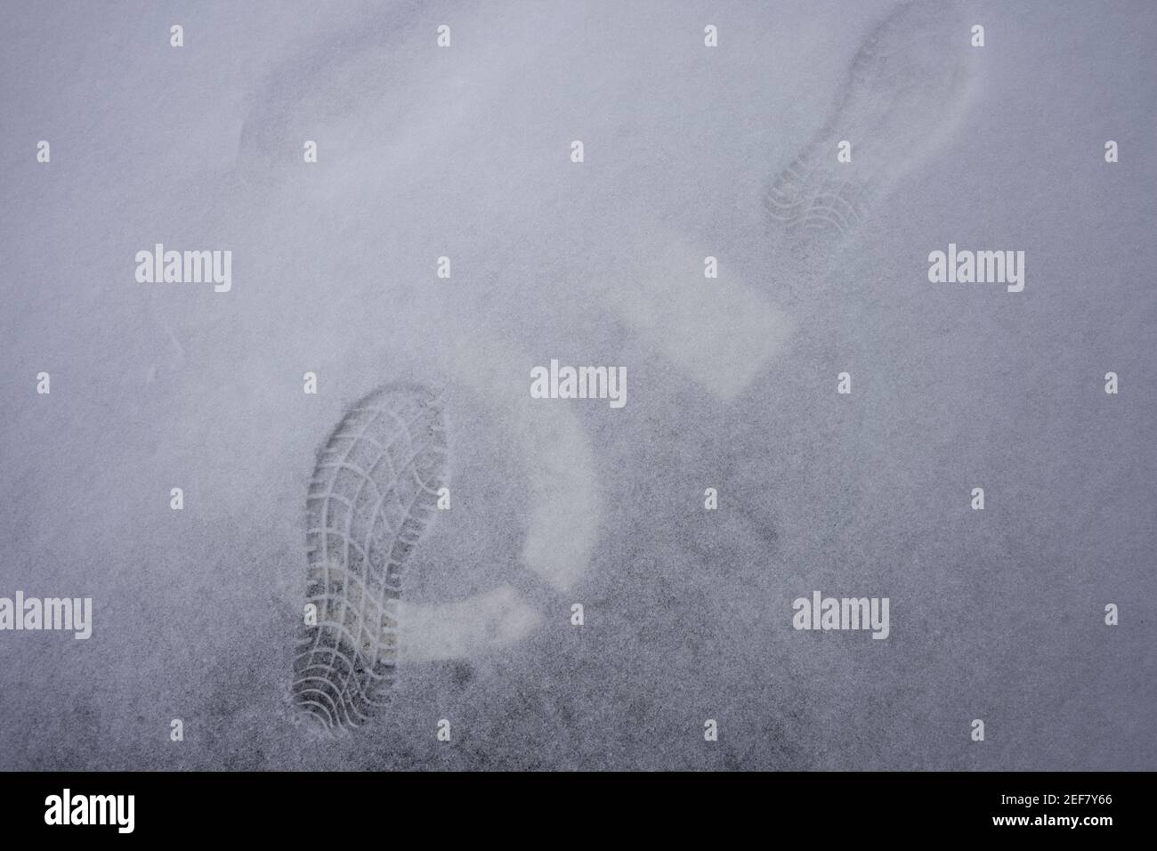 Fußabdrücke, bemalte Parkplatznummermarkierungen und eine dünne Schneeschicht auf dem Boden außerhalb der Garage. Stockfoto