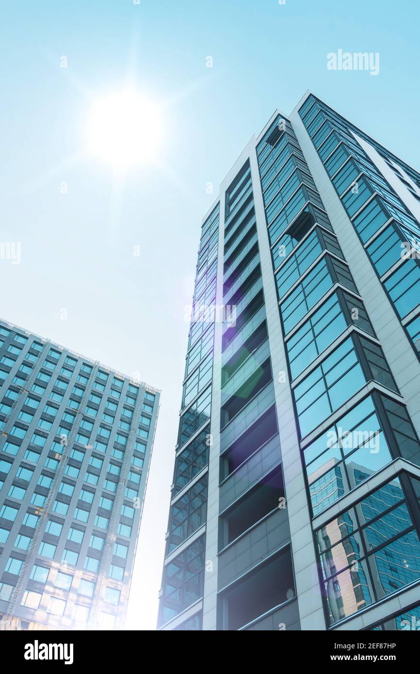 Mehrstöckige Gebäude mit einer Glasfassade und im Bau mit einer Fassadenabteilung, mit einer hellen Sonne am Himmel Stockfoto