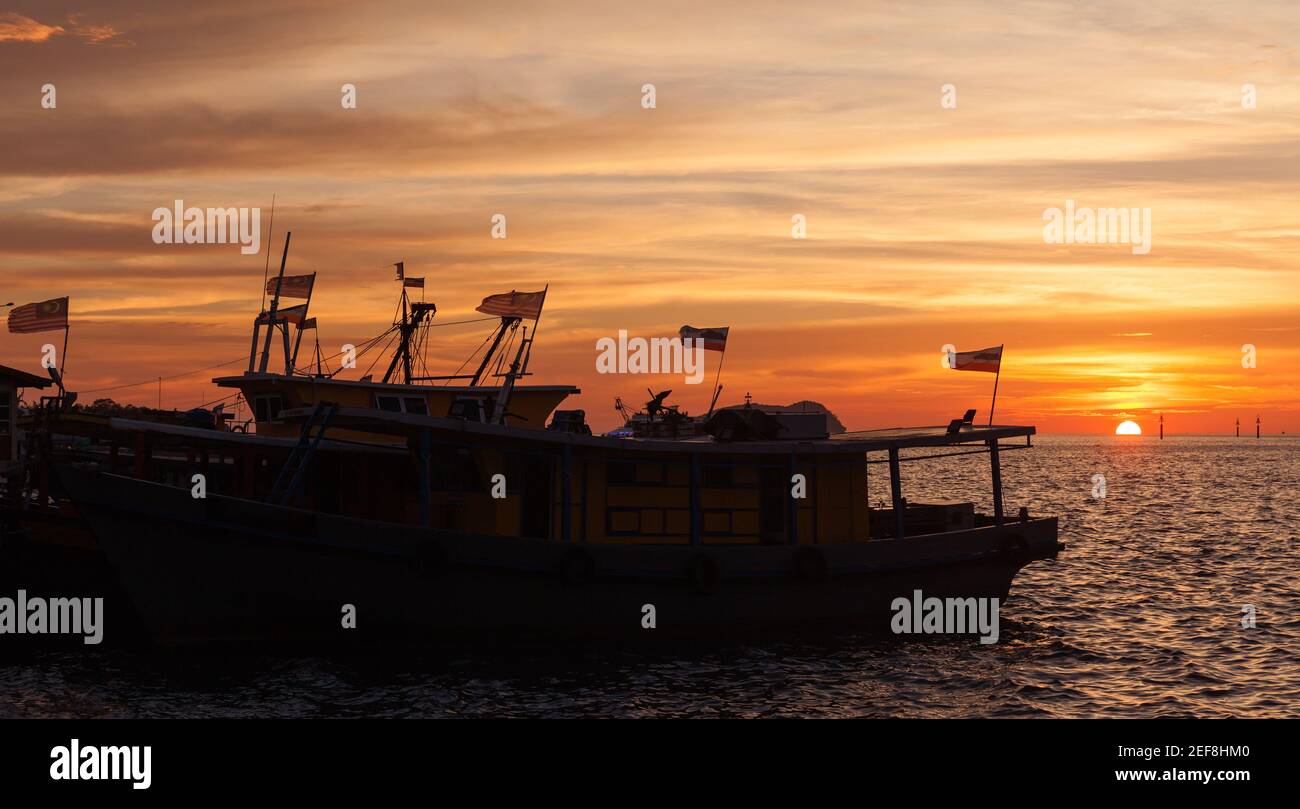 Silhouetten von Fischerbooten mit Fahnen, die in der Nähe von KK Fish festgemacht sind Markt bei Sonnenuntergang Stockfoto