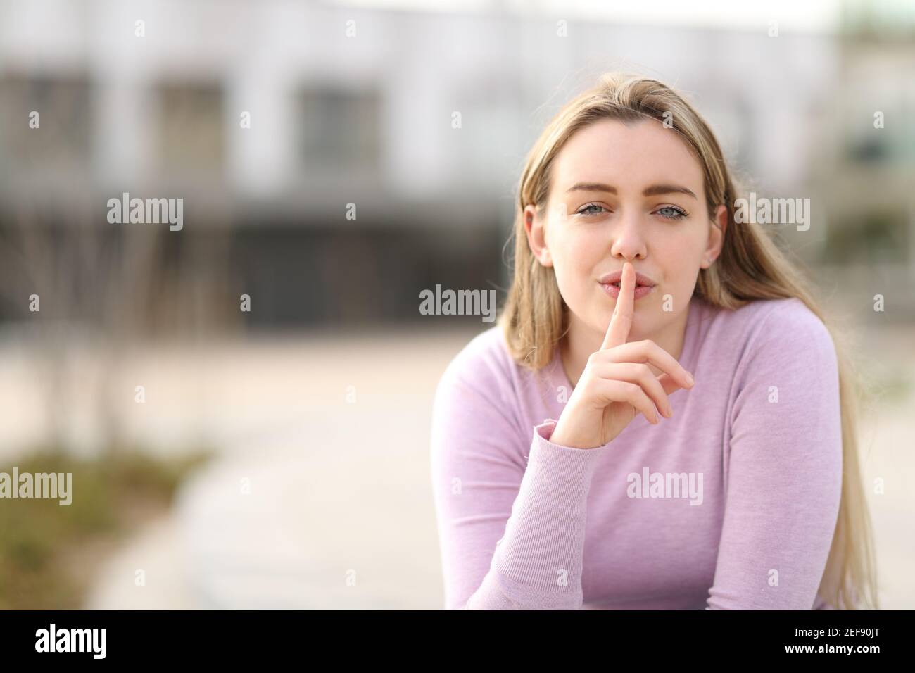 Vorderansicht eines Teenagers, der mit nach Stille fragt Finger auf Lippen draußen auf der Straße Stockfoto