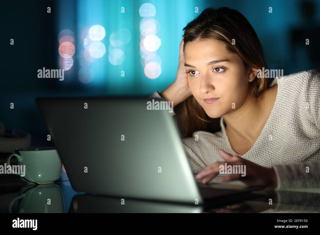 Seriöse Frau, die einen Laptop auf einem Tisch benutzt, um den Inhalt einzuchecken Die Nacht zu Hause Stockfoto