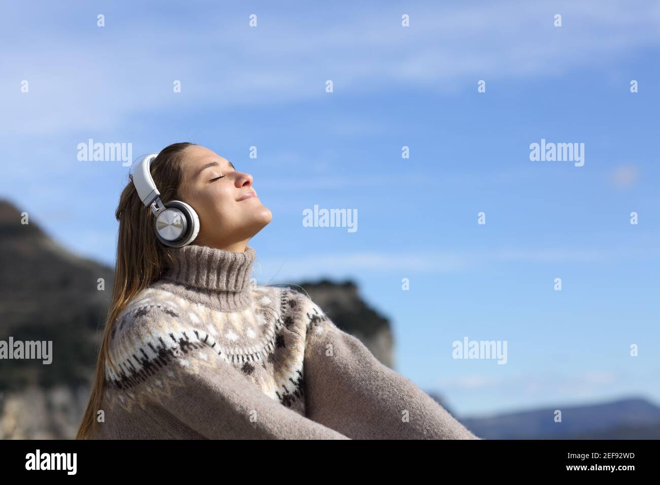 Fröhliche Frau, die mit kabellosen Kopfhörern entspannt Musik hört Der Berg im Winter Stockfoto