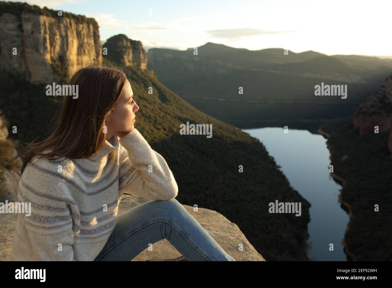 Nachdenkliche Frau, die die Aussicht auf der Spitze einer Klippe betrachtet In den Bergen bei Sonnenuntergang im Winter Stockfoto