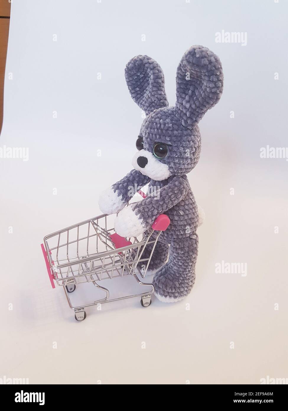 Nahaufnahme von gehäkelten Plüsch Häschen mit leeren Einkaufswagen Spielzeug auf weißem Hintergrund. Stockfoto