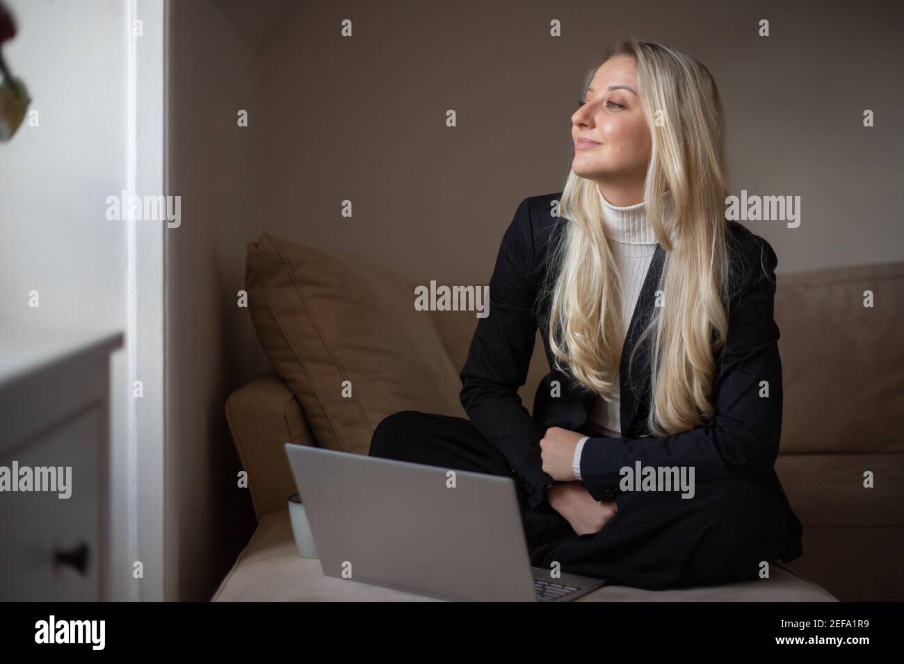 Geschäftsfrau arbeitet von zu Hause aus mit ihrem Laptop online. Sie sitzt auf ihrem Sofa im Wohnzimmer und ist glücklich und positiv. Stockfoto