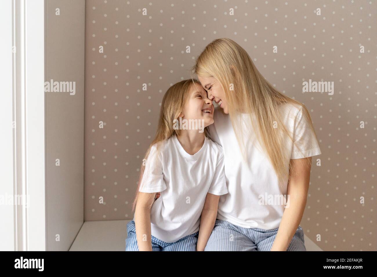 Frau mit kleinen Mädchen zu Hause. Nahaufnahme Porträt, weiße T-Shorts. Mutter und Tochter haben einen Spaß, verwöhnen und lachen. Stockfoto