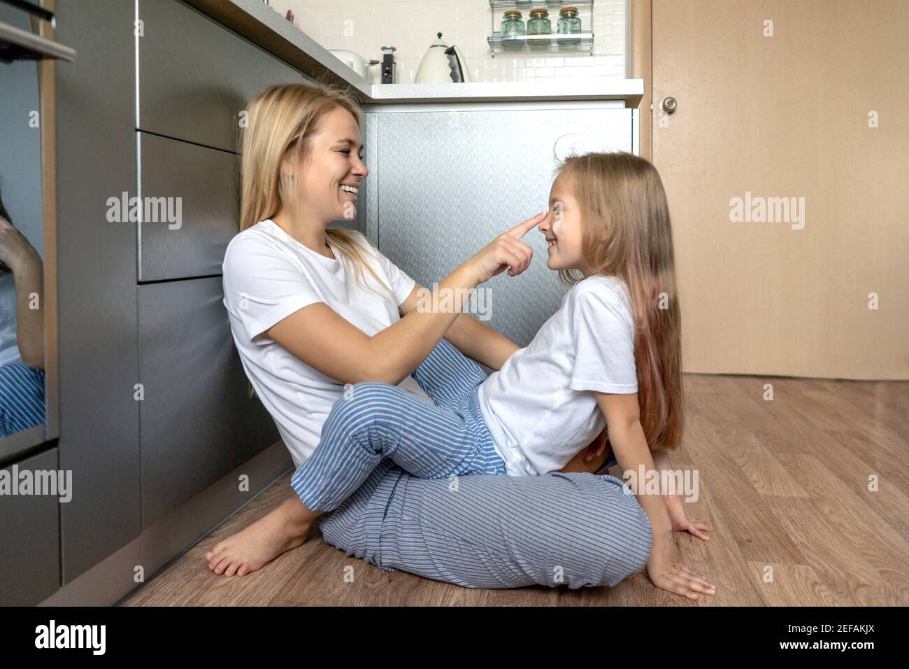 Frau mit kleinen Mädchen zu Hause in der Küche. Nahaufnahme Porträt, weiße T-Shorts. Mutter und Tochter haben einen Spaß, verwöhnen und lachen. Stockfoto
