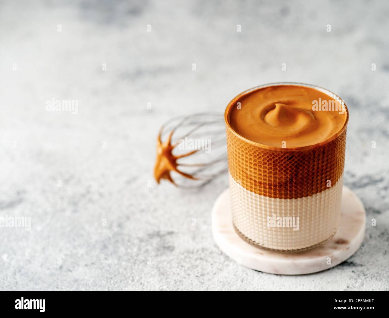 Trendiges koreanisches Getränk - Dalgona Kaffee. Glas mit kalten oder heißen Getränken - Schlagsahne Instant-Kaffee mit Milch und Schneebesen auf grauem Zement Hintergrund mit Kopierraum für Text oder Design Stockfoto
