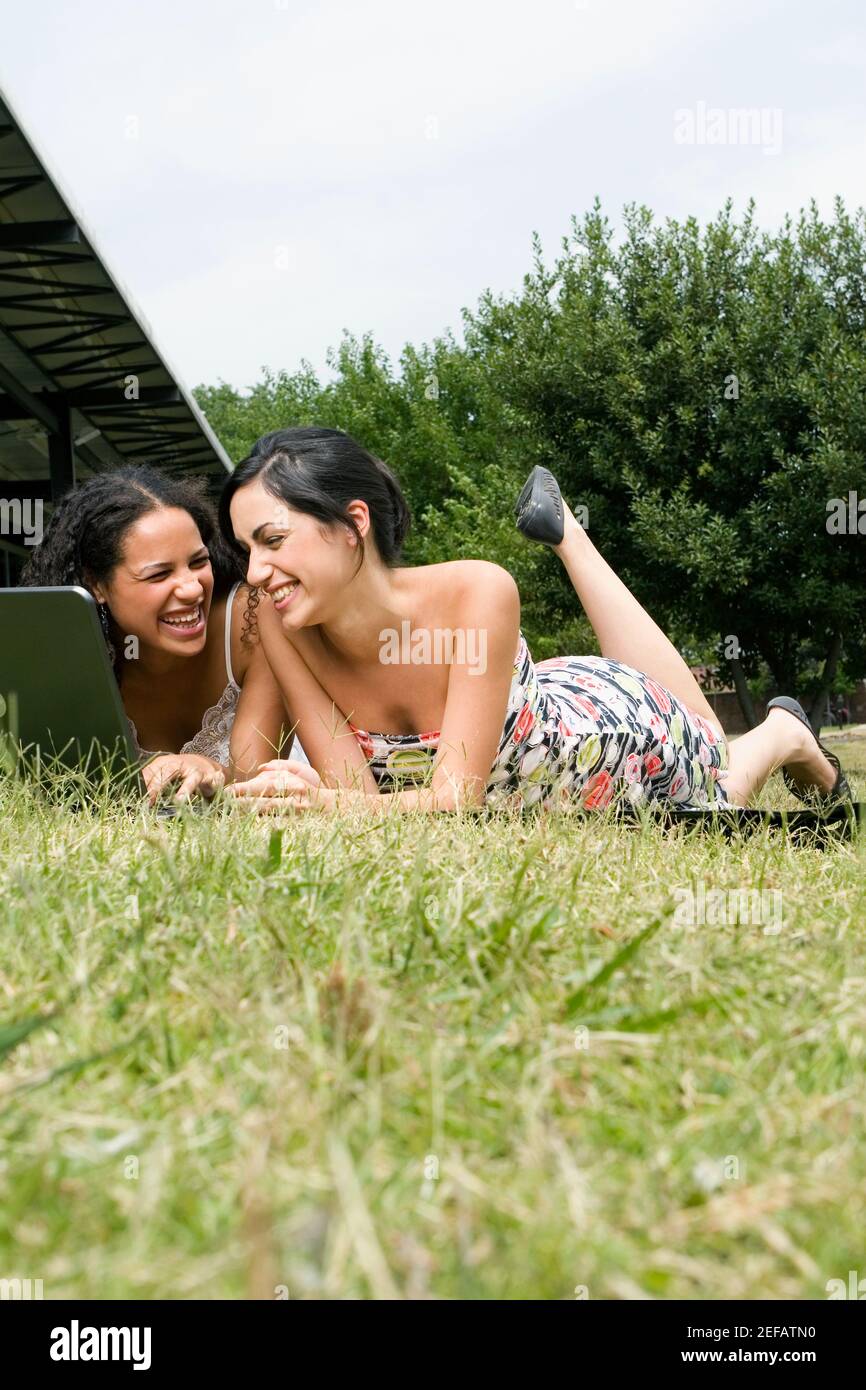 Zwei Studentinnen liegen vor einem Laptop In einem Rasen Stockfoto