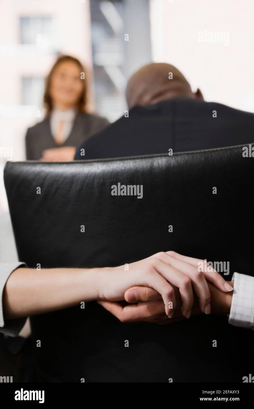 Nahaufnahme einer manÅ½s Hand, die eine womanÅ½s Hand hinter sich hält Ein Stuhl in einem Büro Stockfoto