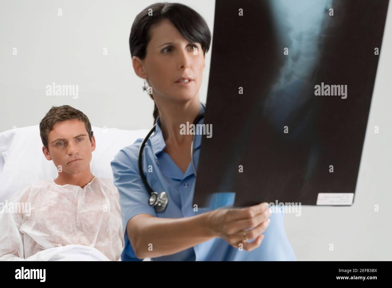 Weibliche Chirurgen, die einen Röntgenbericht mit einem Patienten in untersuchen Der Hintergrund Stockfoto