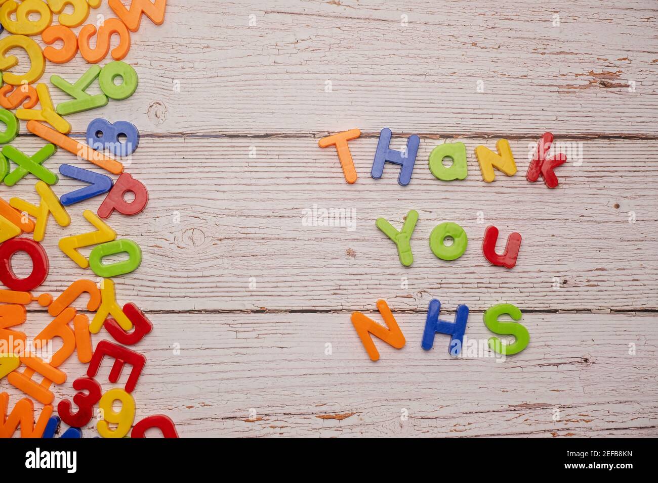 Bunte Magnetbriefe auf einem rustikalen weißen Tisch zu Hause Schule Coronavirus Rechtschreibung Danke NHS Stockfoto