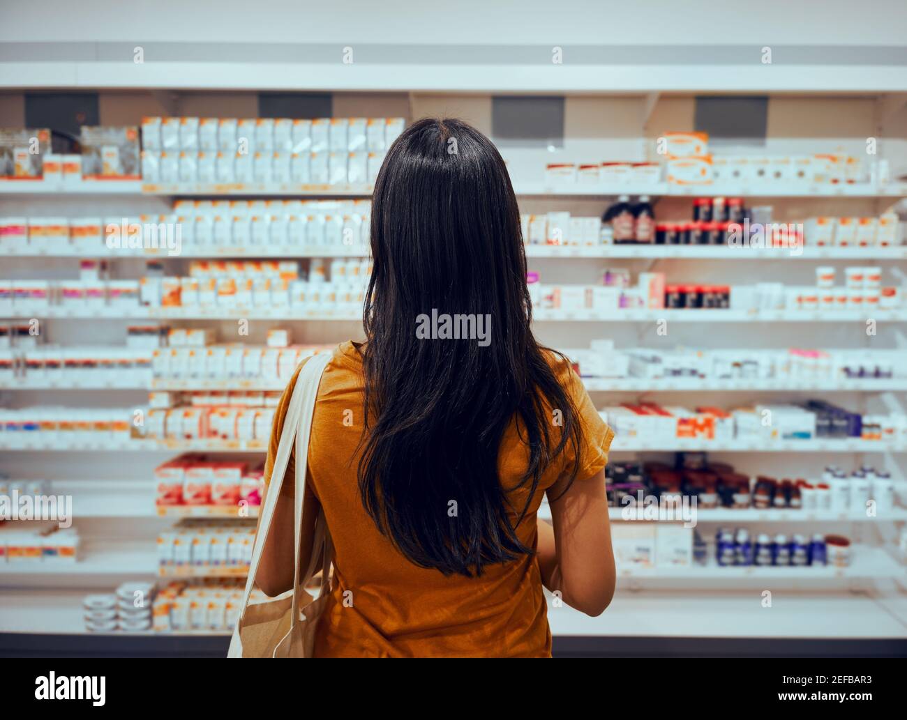 Rückansicht einer jungen Frau mit Tasche, die gegen das Regal steht In der Apotheke auf der Suche nach Medizin Stockfoto