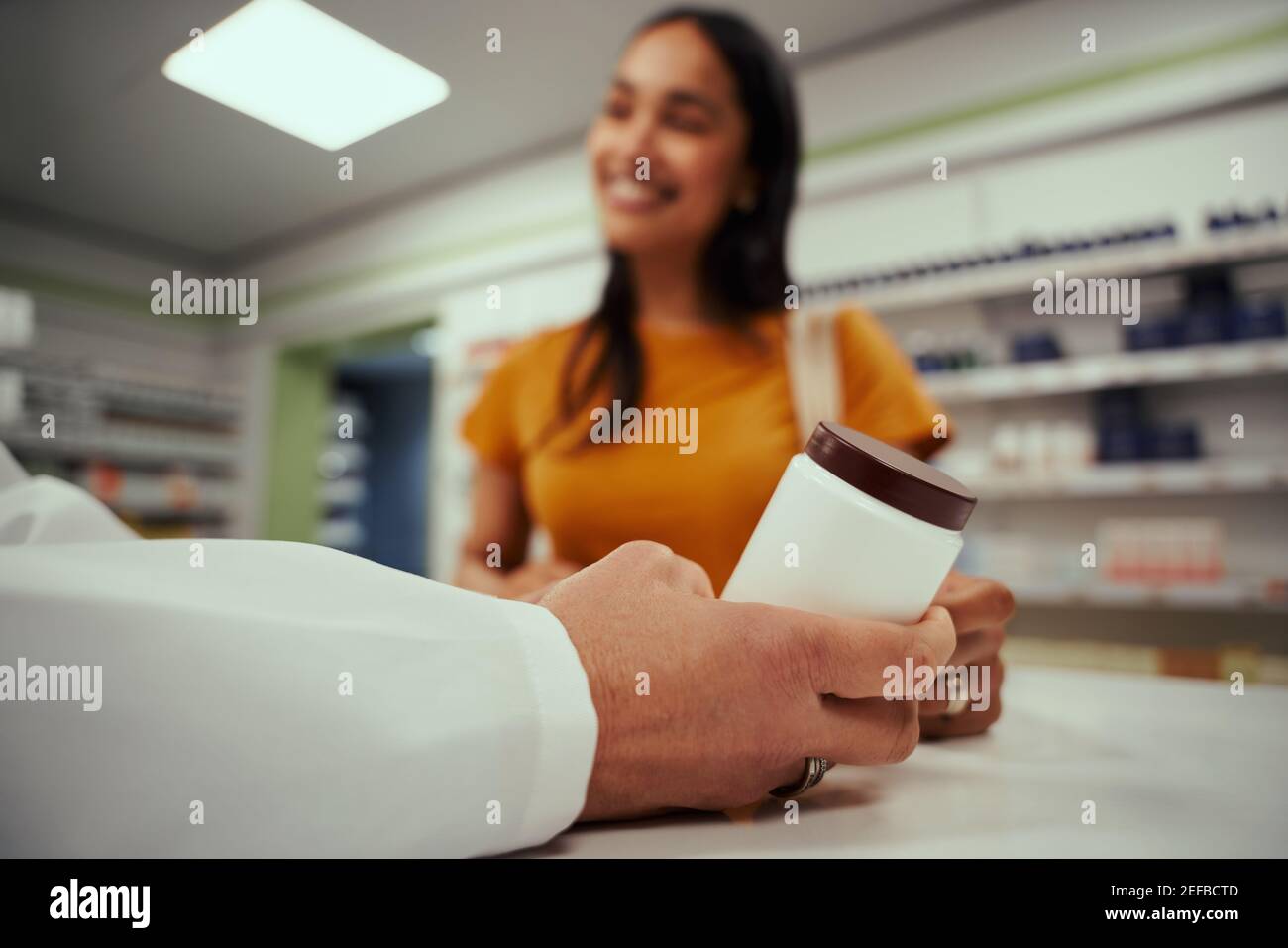 Nahaufnahme der Hände der älteren Apothekerin mit Flasche Ergänzungen an der Apotheke Schalter, während Frau auf den Kauf wartet Stockfoto