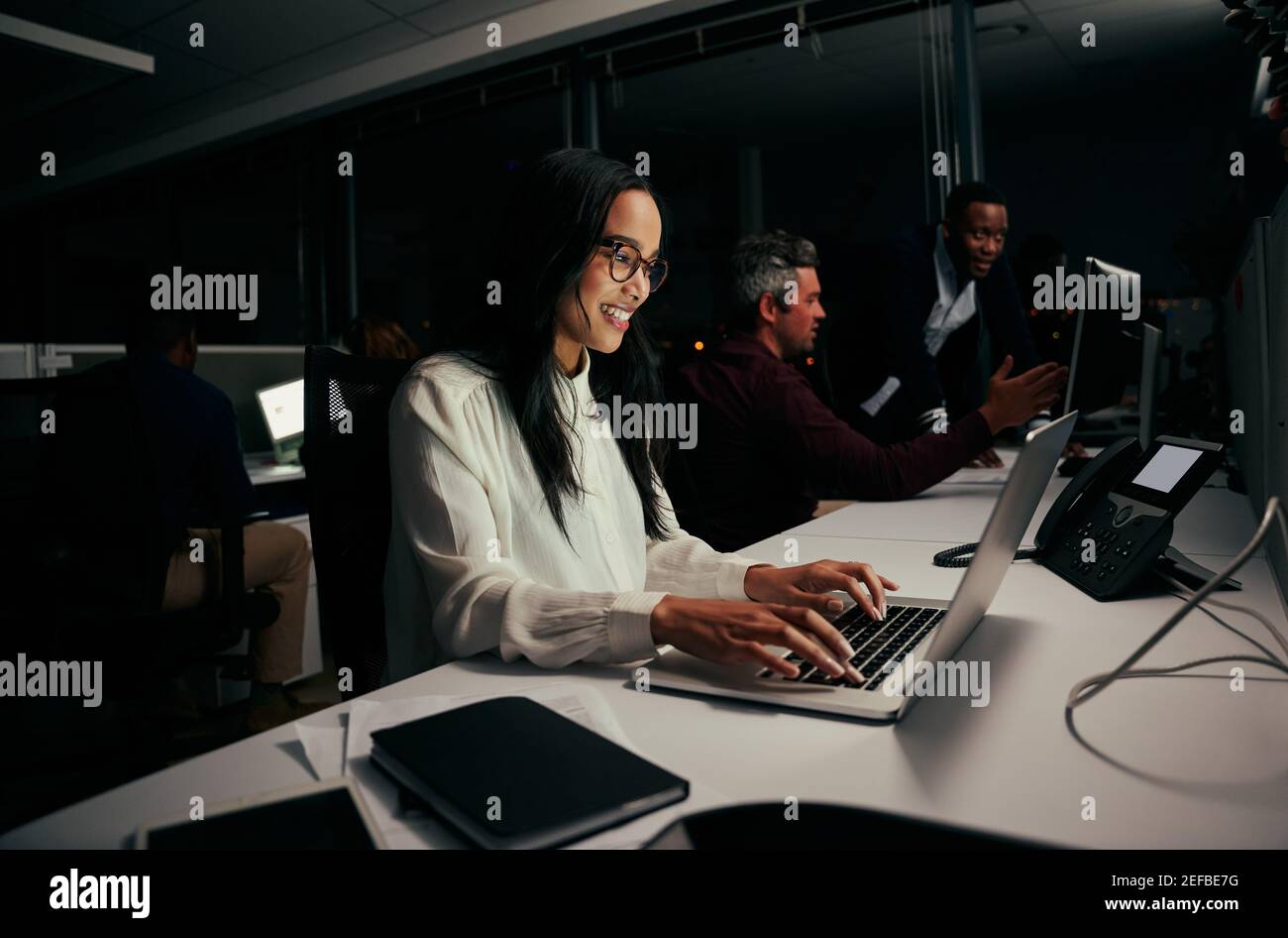 Weibliche Angestellte beschäftigt in ihrer Arbeit auf Laptop im Büro Und mit Kollegen im Hintergrund Stockfoto