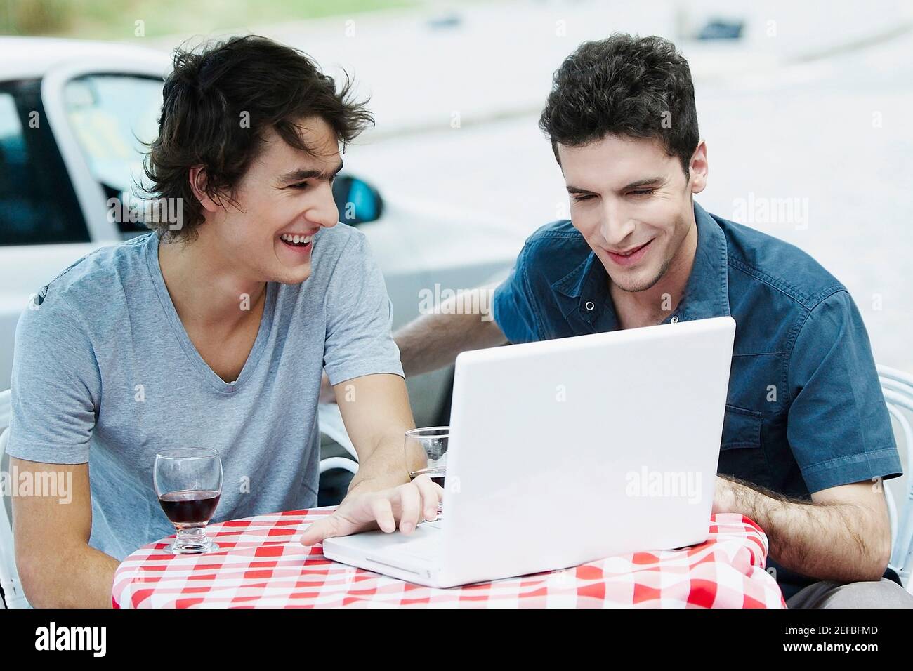 Zwei junge Männer, die einen Laptop benutzen und lächeln Stockfoto