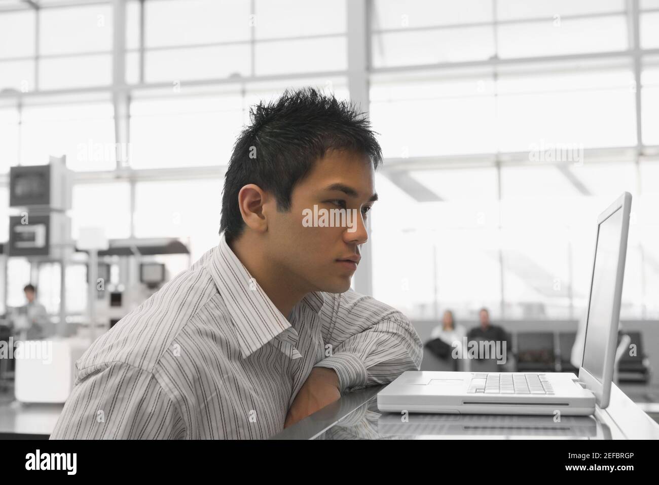 Seitenprofil eines Geschäftsmannes, der einen Laptop ansieht Ein Check-in-Schalter am Flughafen Stockfoto