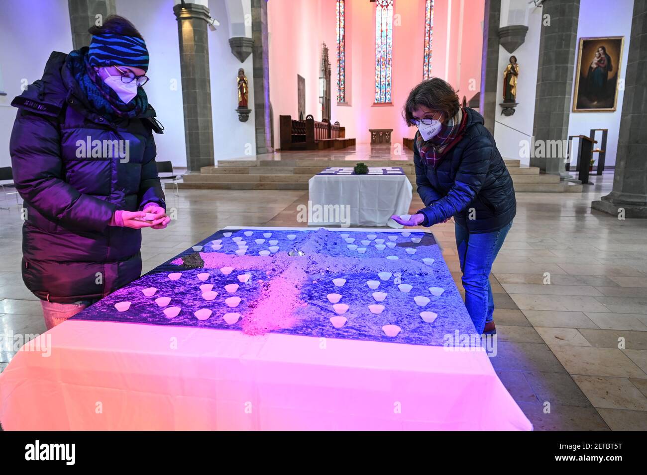 Ravensburg, Deutschland. Februar 2021, 17th. Zwei Gläubige nehmen jeweils eine mit Asche gefüllte Muffin-Dose von einem Tisch in der Pfarrkirche St. Jodok, um danach das Aschekreuz auf ihren Stirnen zu machen. Um die Tradition des Aschenkreuzes gemäß den Corona-Regeln umzusetzen, füllten die Organisatoren die Asche in Muffin-Dosen, so dass der Abstand eingehalten werden kann. Quelle: Felix Kästle/dpa/Alamy Live News Stockfoto