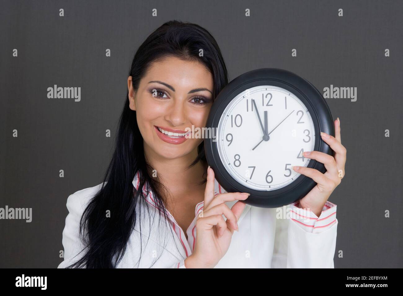 Nahaufnahme einer Geschäftsfrau, die eine Uhr hält und lächelt Stockfoto