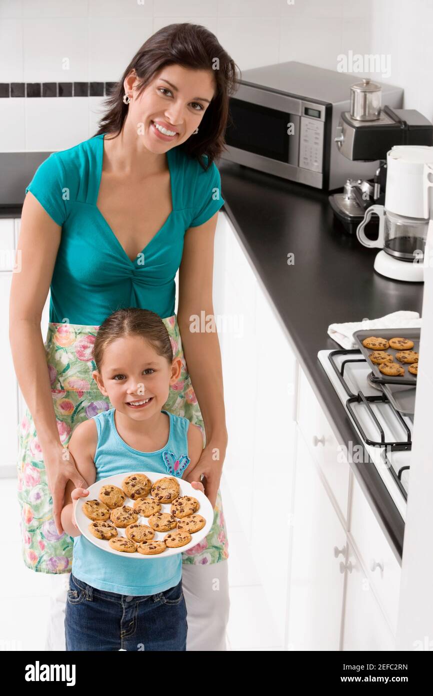 Junge Frau mit ihrer Tochter, die einen Plätzchen hält In der Küche Stockfoto