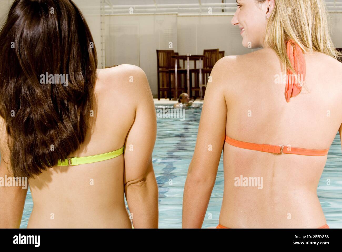 Rückansicht von zwei jungen Frauen, die am Rand sitzen Eines Schwimmbades Stockfoto