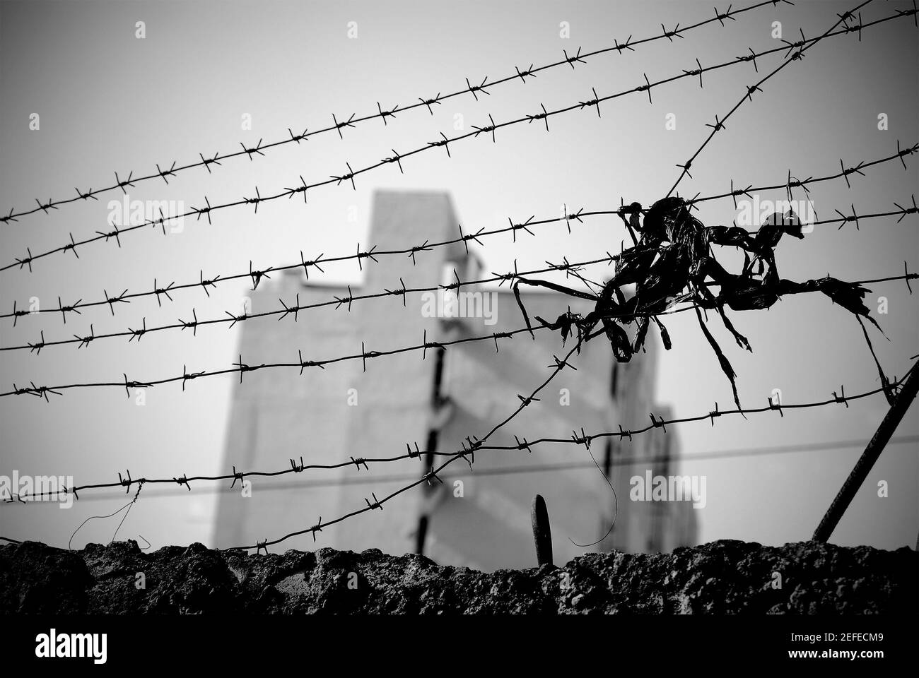 Stacheldraht streckte sich über die Wand mit einem mehrstöckigen Gebäude, das weit weg in Unschärfe zu sehen war. Stockfoto