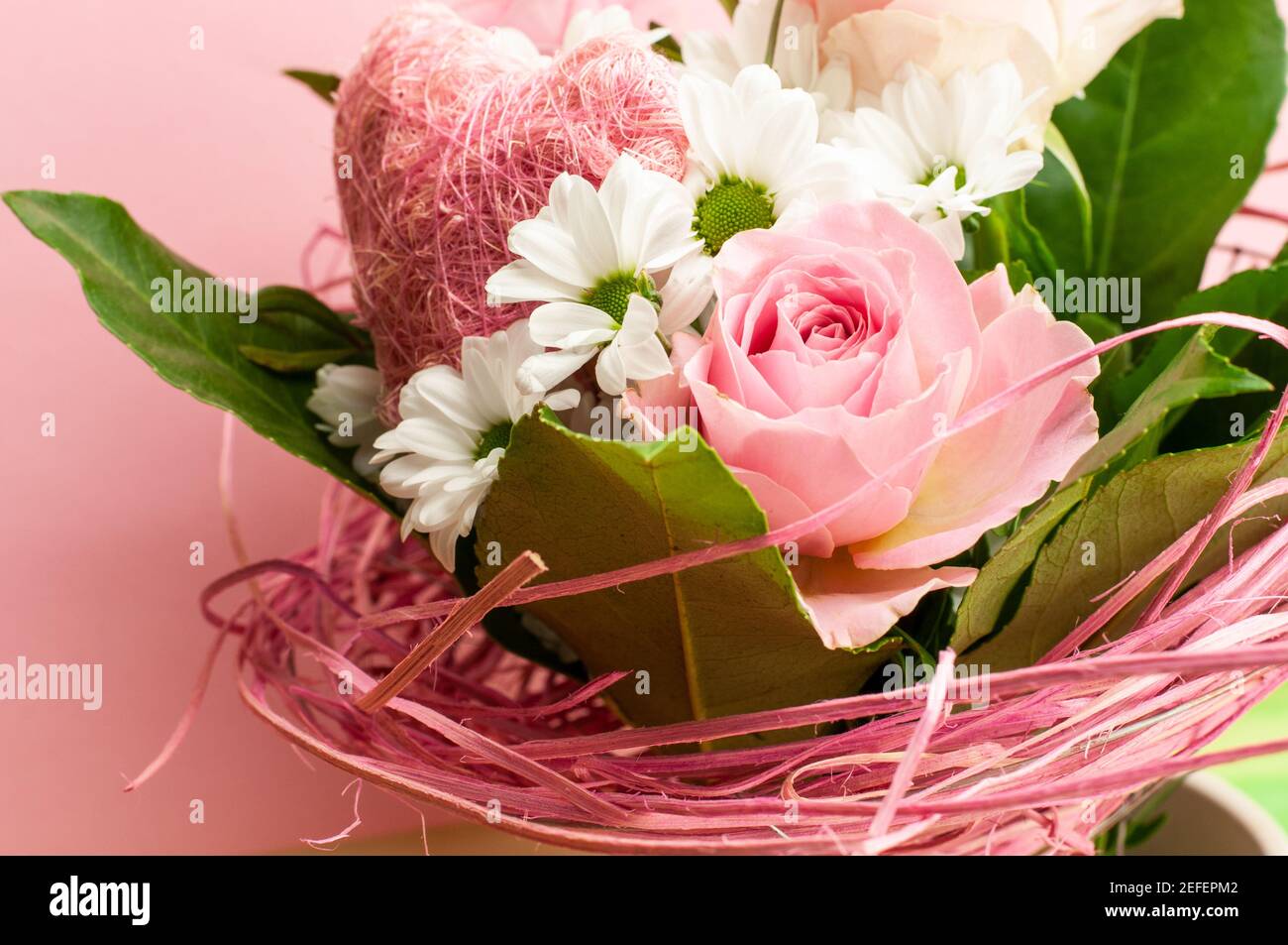 Ein Bouquet mit rosa Rosen und weißen Gänseblümchen verziert mit Holzfasern und ein Herz aus Saiten Stockfoto