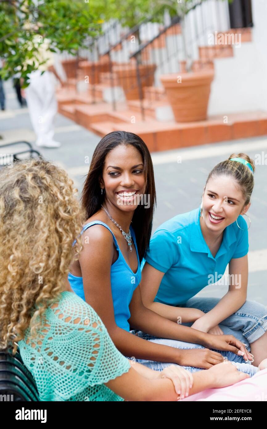 Drei Mädchen im Teenageralter sitzen auf einer Bank und lächeln Stockfoto