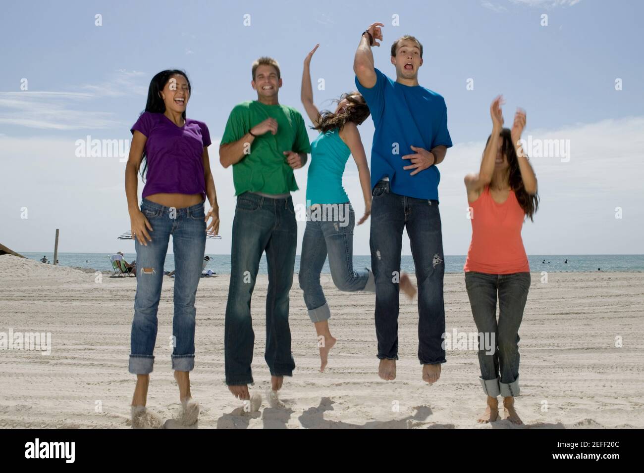 Drei junge Frauen und zwei junge Männer springen auf die Strand Stockfoto