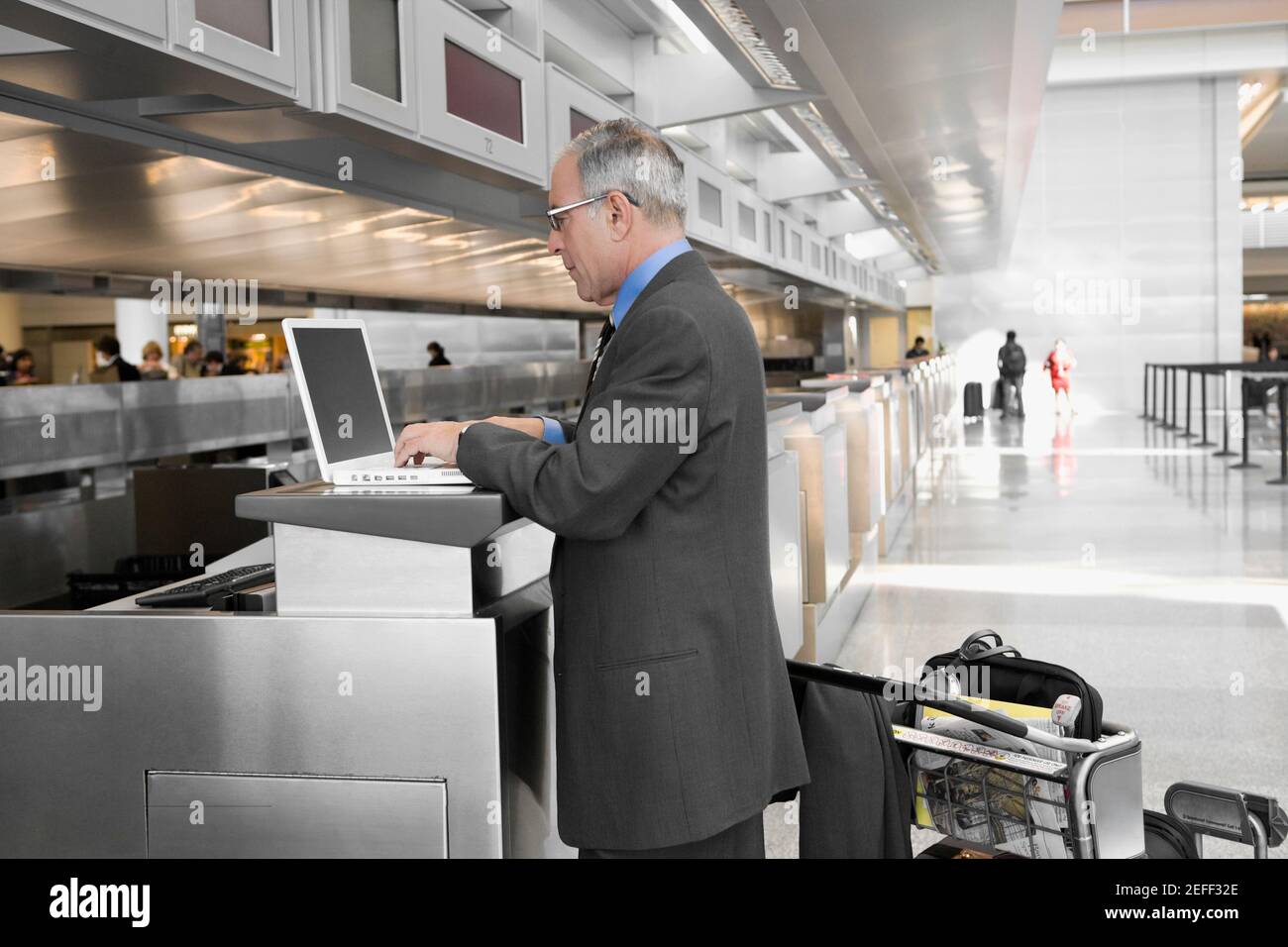 Seitenprofil eines Geschäftsmannes, der einen Laptop bei einem verwendet check-in-Schalter am flughafen Stockfoto
