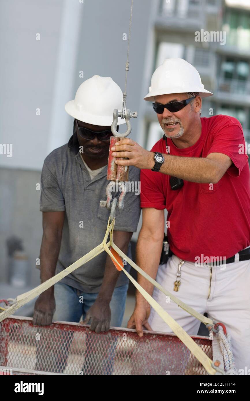 Zwei manuelle Arbeiter befestigen einen Behälter in den Haken von Ein Aufzug Stockfoto
