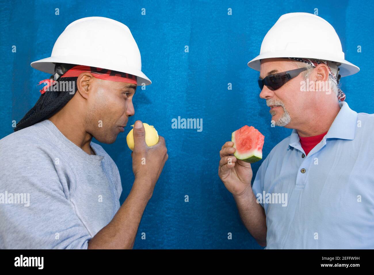 Nahaufnahme von zwei männlichen Bauarbeitern von Angesicht zu Angesicht und Obst essen Stockfoto