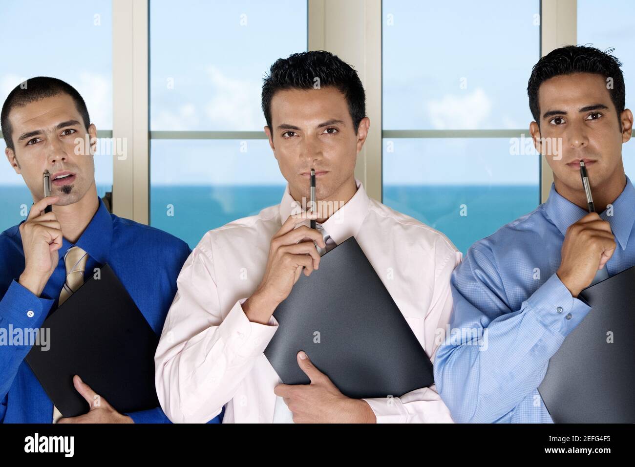Porträt von drei Geschäftsleuten, die Stifte an ihren Gesichtern halten Stockfoto