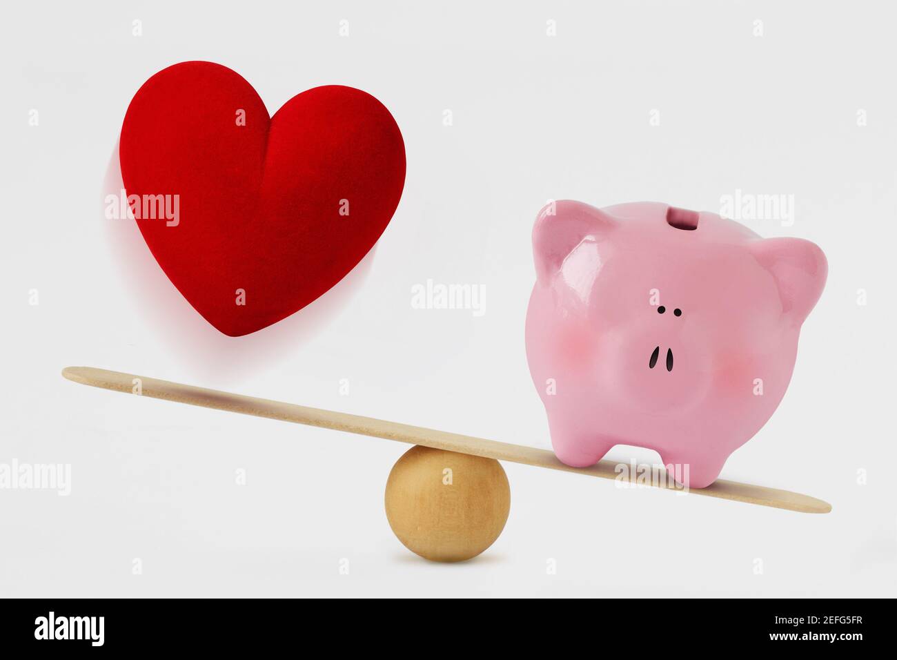 Herz und Sparschwein auf Waage - Konzept der Reichtum Vorrang vor Liebe im Leben Stockfoto