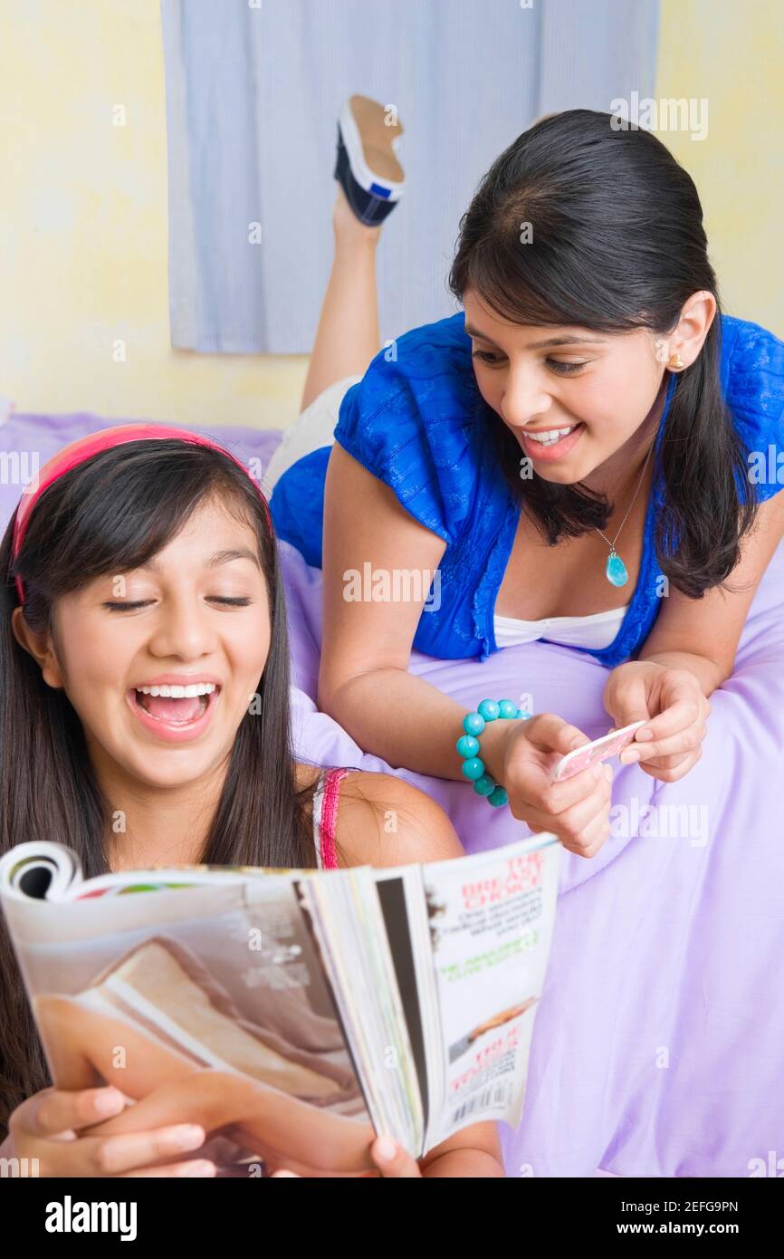 Teenager-Mädchen Lesen einer Zeitschrift mit einer jungen Frau, die hinter ihr auf dem Bett liegend Stockfoto