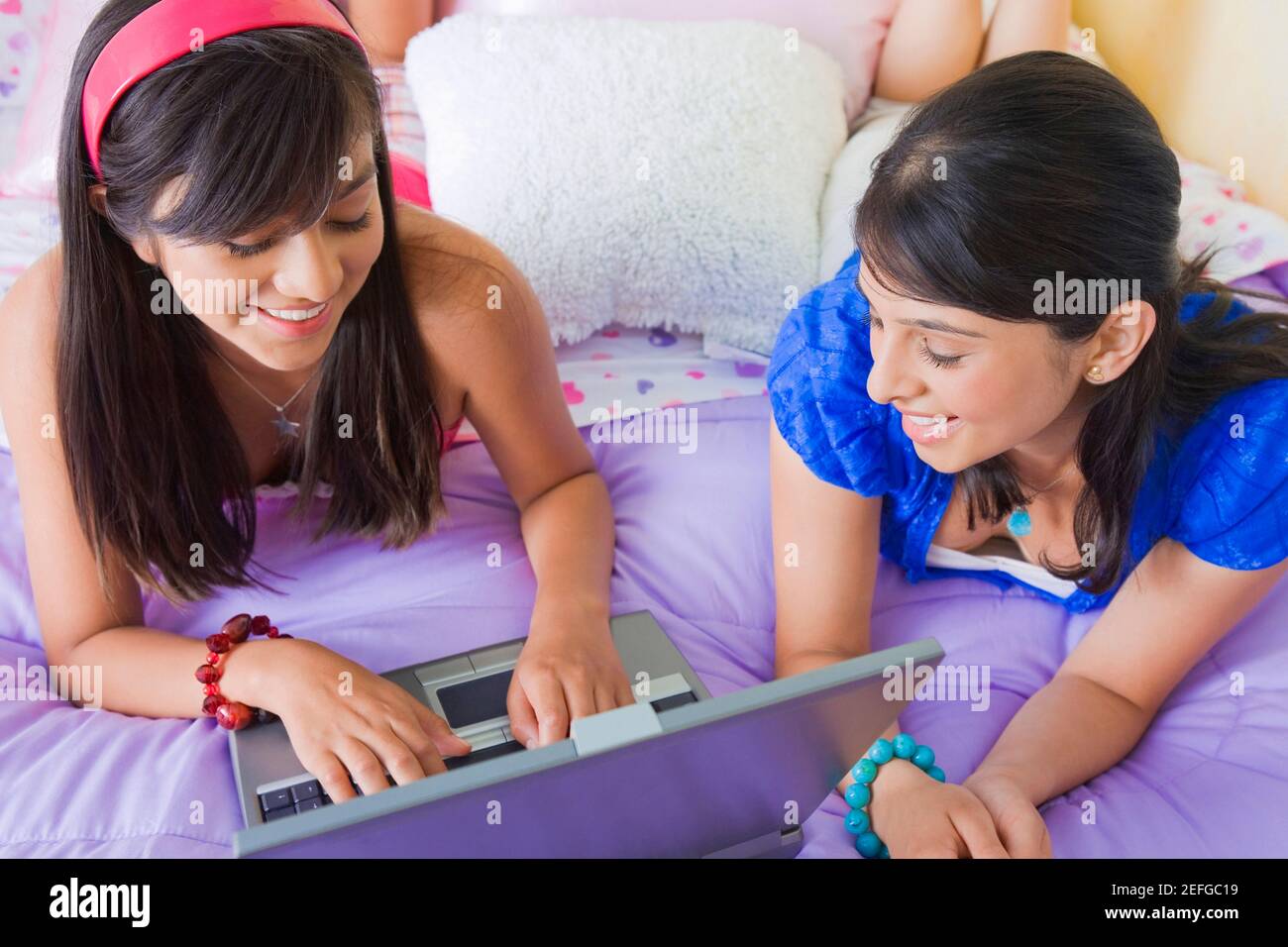 Teenager-Mädchen auf einem Laptop mit einer jungen Frau, die neben ihr auf dem Bett liegend arbeiten Stockfoto