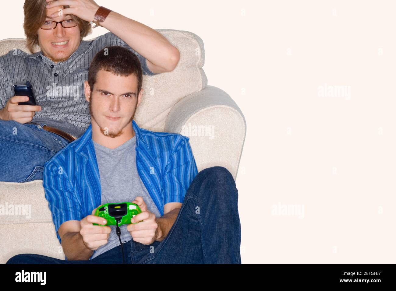 Junger Mann mit einem anderen jungen Mann mit einem Mobiltelefon hinter ihm spielen Videospiel Stockfoto