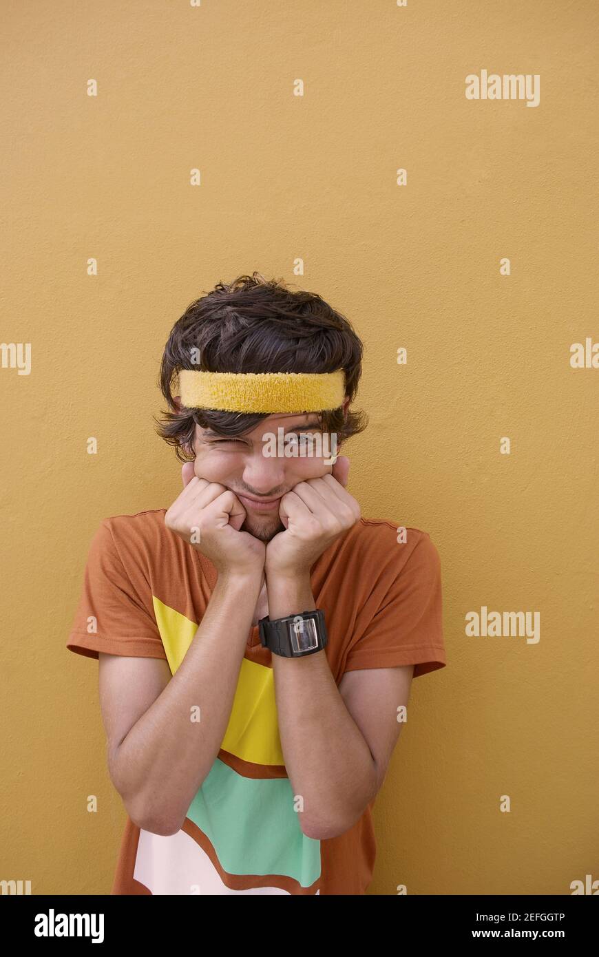 Junger Mann stehend mit den Händen am Kinn und Grimasse Stockfoto