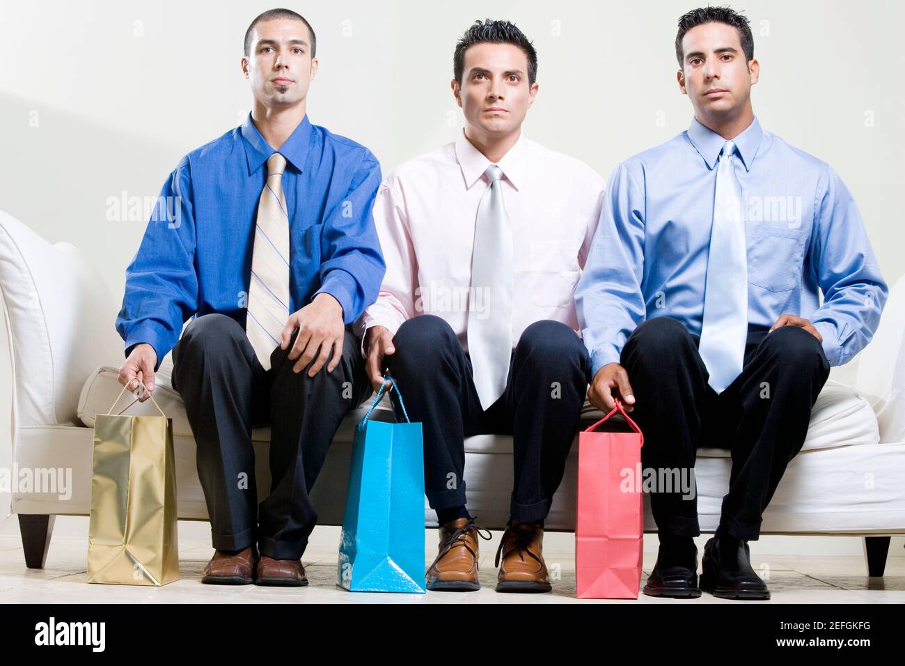 Zwei junge Männer und ein mittelalter Mann sitzen darauf Eine Couch mit Einkaufstaschen Stockfoto